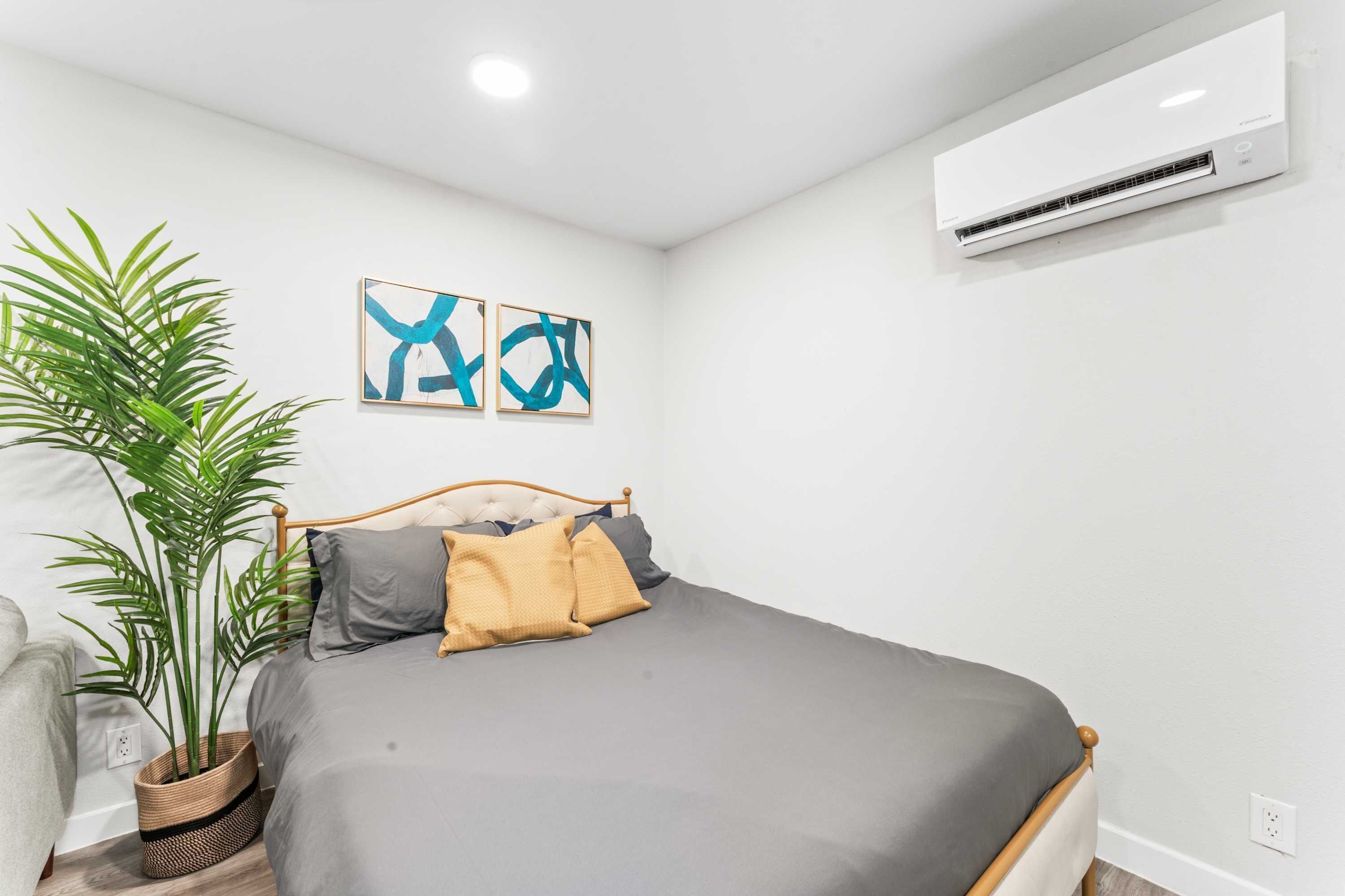 A bedroom with a bed, a potted plant, and an air conditioning unit on the wall.