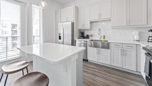 A modern kitchen with white cabinets, a stainless steel refrigerator, and a central island with stools. - Chic West Downtown Studio w Washer Dryer (Austin)