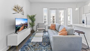 A modern living room with a sofa, TV, and a large window. - Boho Soco 1BR Queen Suite w Gympickleballlaundry (Austin)
