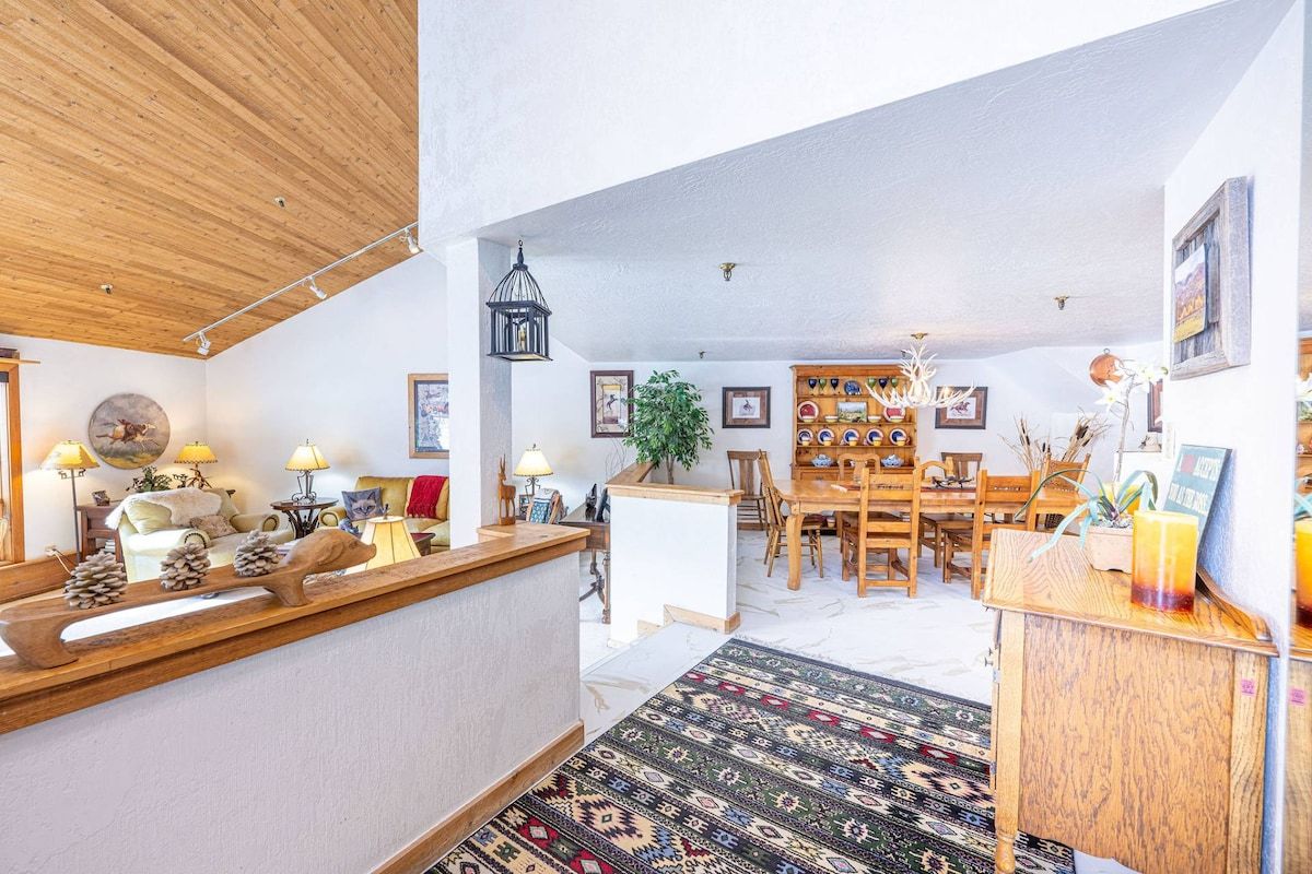 A modern interior with a wooden reception desk, a patterned rug, and a dining area with wooden furniture.