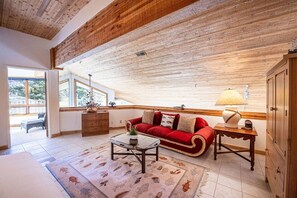 Ein gemütliches Wohnzimmer mit Holzbalkendecke, einem roten Sofa, einem Couchtisch und einer Lampe.
