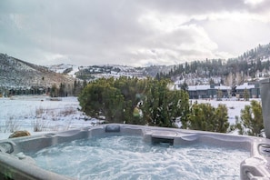 Ein Whirlpool mit Blick auf eine verschneite Landschaft und ein Gebäude im Hintergrund.