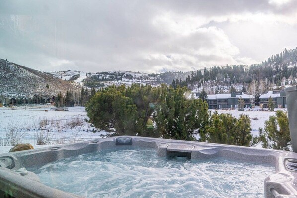 Ein Whirlpool mit Blick auf eine verschneite Landschaft und ein Gebäude im Hintergrund.
