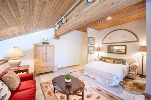 Ein Schlafzimmer mit Holzboden, einem Bett mit weißer Bettwäsche, einem roten Sofa, einem Holzschrank und einem kleinen Tisch mit einer Pflanze.