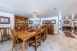 Uma área de refeições com mesa e cadeiras de madeira, um lustre e uma vitrine na parede com pratos e cerâmica.