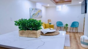 A modern living room with a marble table, a wooden planter with green plants, a yellow sofa, and two blue chairs. - Unique, Modern and Lovely Space! (East Providence)