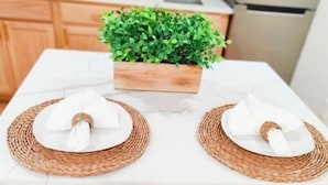 A kitchen with a white countertop, two woven placemats, a potted plant, and a two-seater bench. - Unique, Modern and Lovely Space! (East Providence)