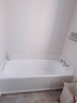 Une salle de bain avec une baignoire blanche, un petit vase en verre contenant des tiges de roseaux et un porte-serviettes.