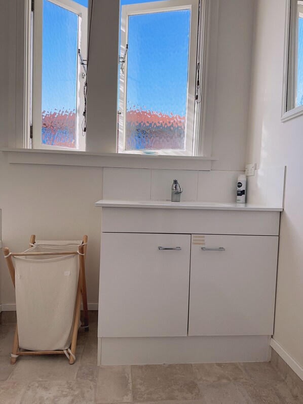 Una habitación con un armario blanco, un lavamanos pequeño y una ventana con vistas a árboles.