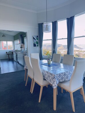 Un coin repas avec une table dressée pour quatre personnes, entourée de chaises blanches, dans une pièce offrant une vue sur un paysage montagneux grâce à de grandes fenêtres.