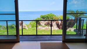 Une pièce avec vue sur l’océan grâce à de grandes fenêtres, un balcon avec une balustrade et un plancher en bois.