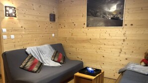 Een gezellig kamer in een blokhut, met houten inrichting, een bank met kussens, een kleine tafel en een bed.