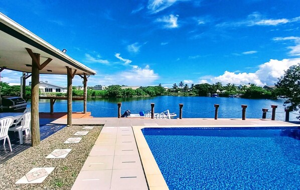 A swimming pool with a view of a lake and a covered patio area with chairs. - Waterfront Sunset Apt Fantasy Island (Nadi)