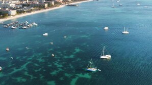 An aerial view of a coastal area with clear turquoise waters, boats, and a marina.