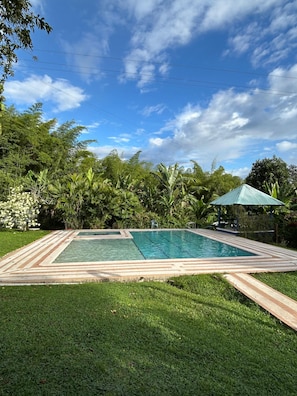 A rectangular swimming pool with a tiled deck, surrounded by lush greenery and a clear blue sky. - El Prado EcoHotel (Montenegro)