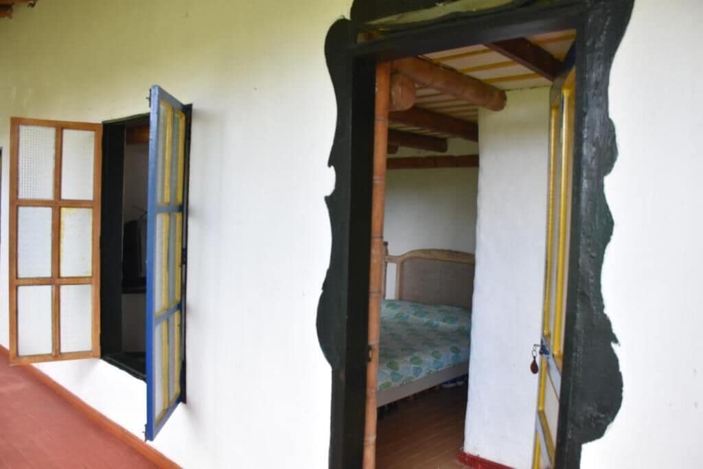 Ein Zimmer mit einem Bett, einer Holztür und einem Fenster mit blauem Rahmen.