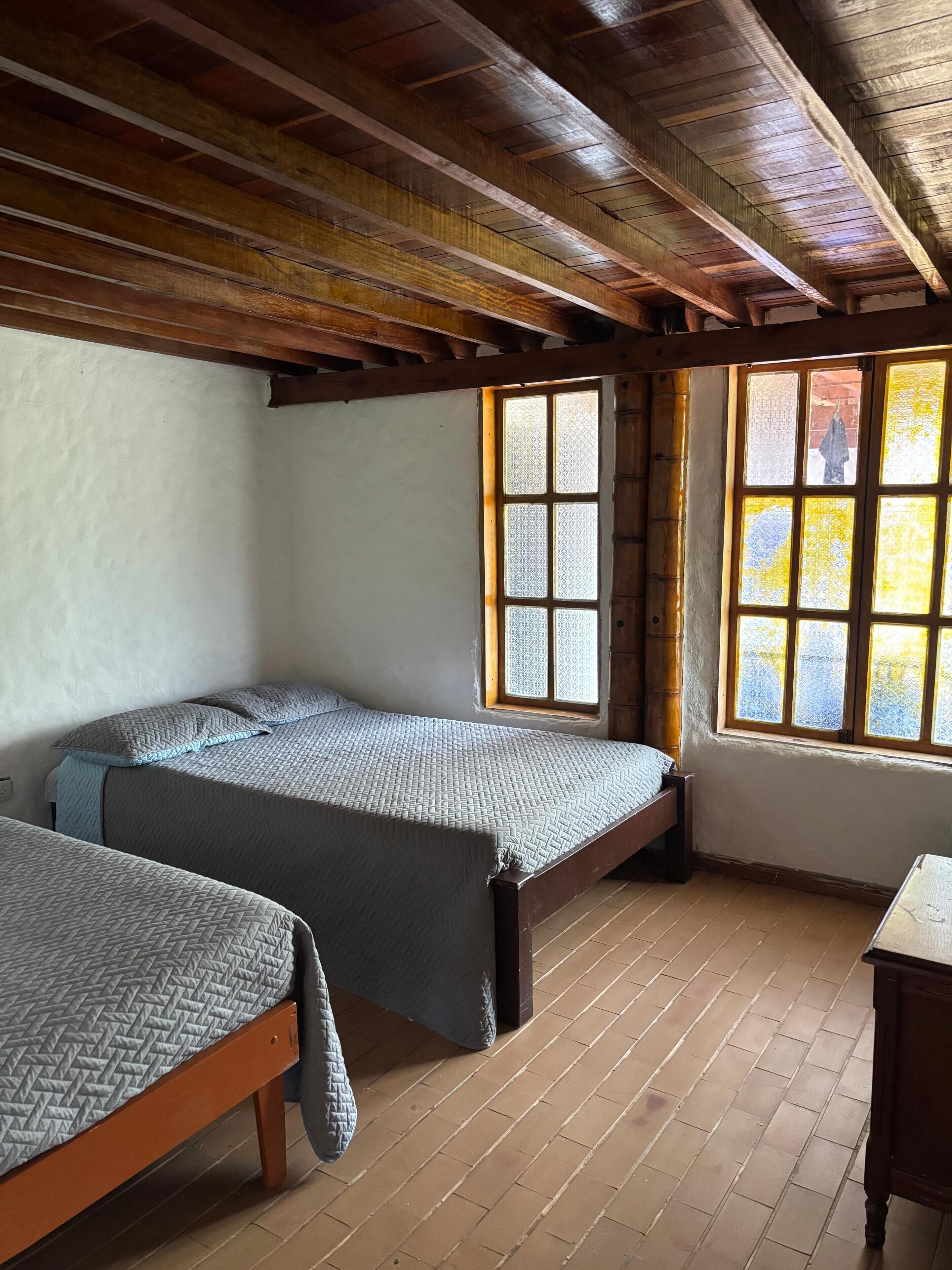A room with two wooden beds, a window with patterned glass, and a wooden ceiling.