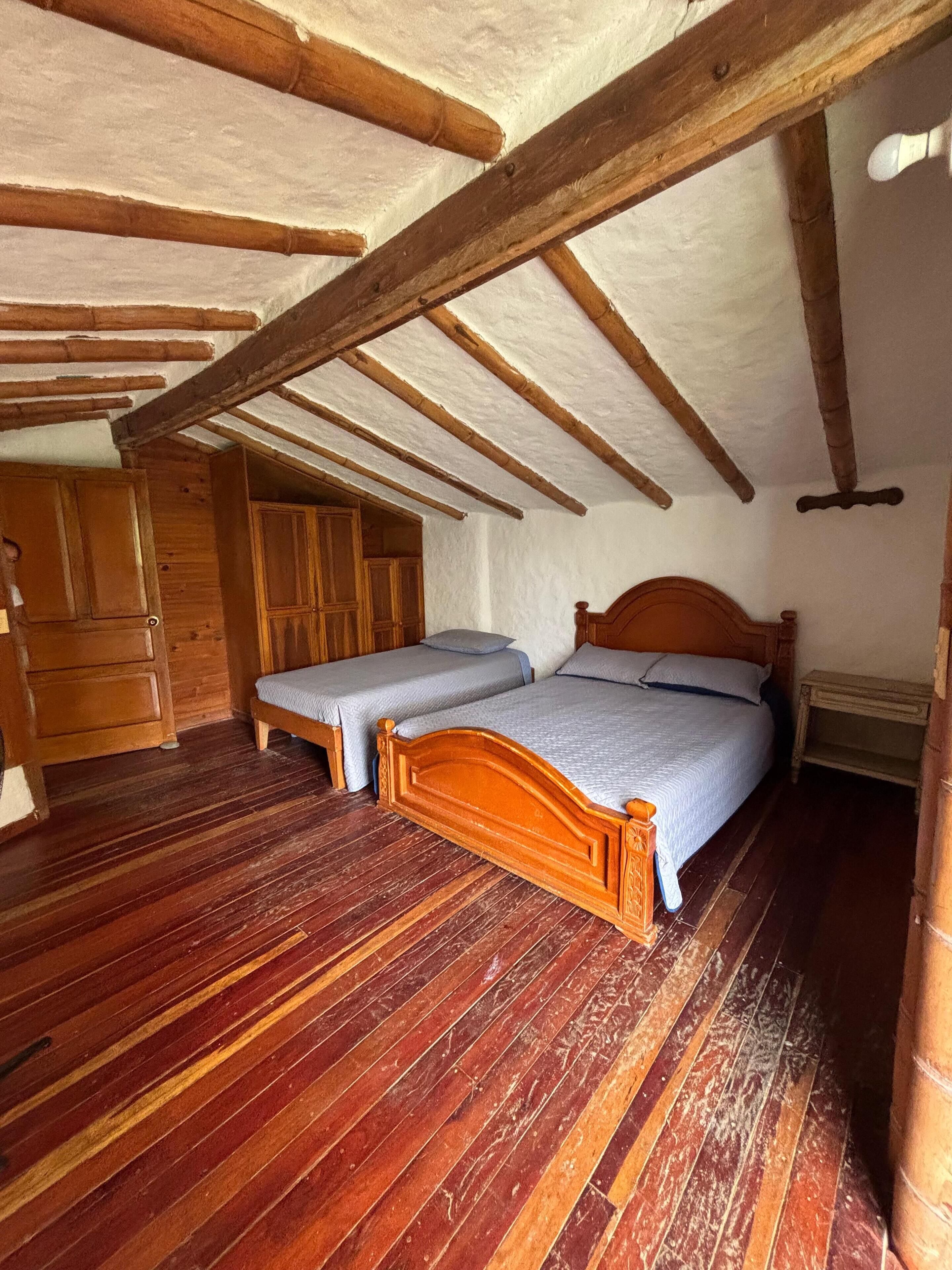 Une pièce rustique en bois, avec deux lits, des poutres apparentes au plafond et un plancher en bois.