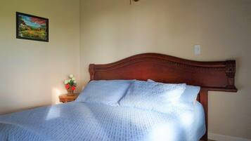 A bedroom with a wooden headboard, a bed with a blue quilt, a nightstand with a vase of flowers, and a painting on the wall.