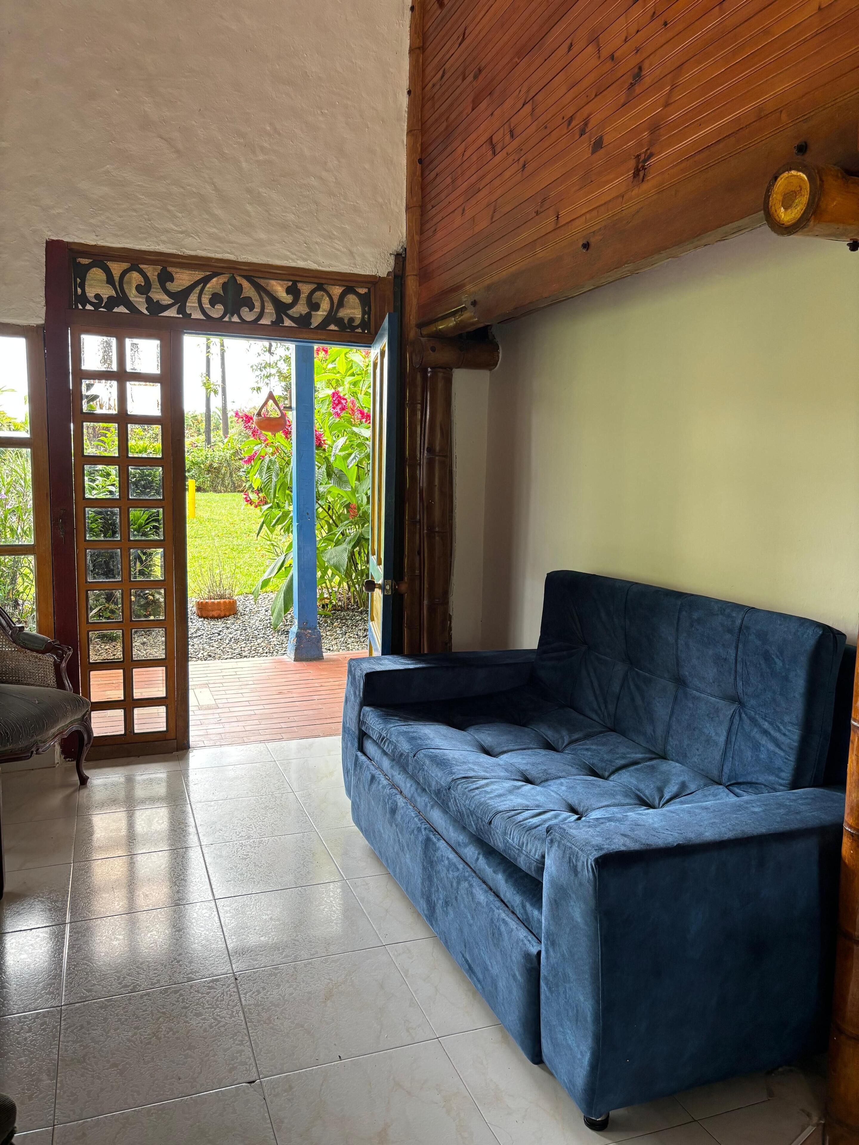 Una habitación con un sofá azul, techo de madera y una puerta que da a un jardín.