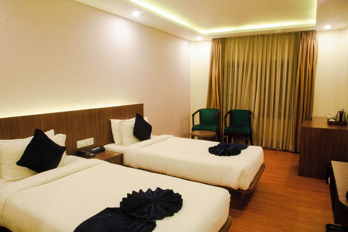 Habitación de hotel con dos camas, un escritorio, una silla y una cortina.
