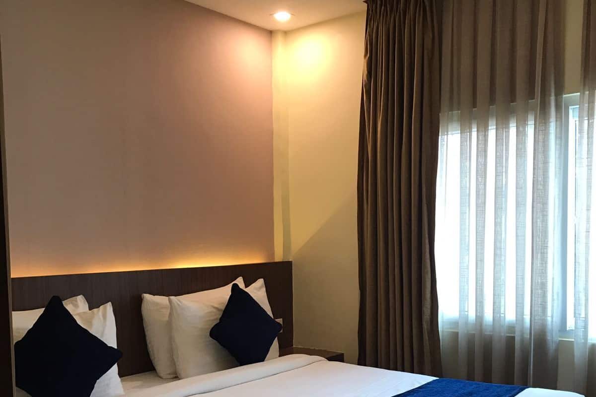 Habitación de hotel con una cama grande, cabecera y ventana con cortinas.