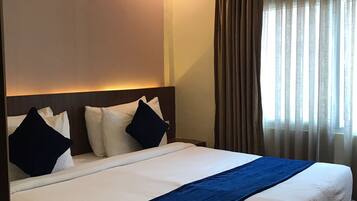 Habitación de hotel con una cama grande, cabecera y ventana con cortinas.