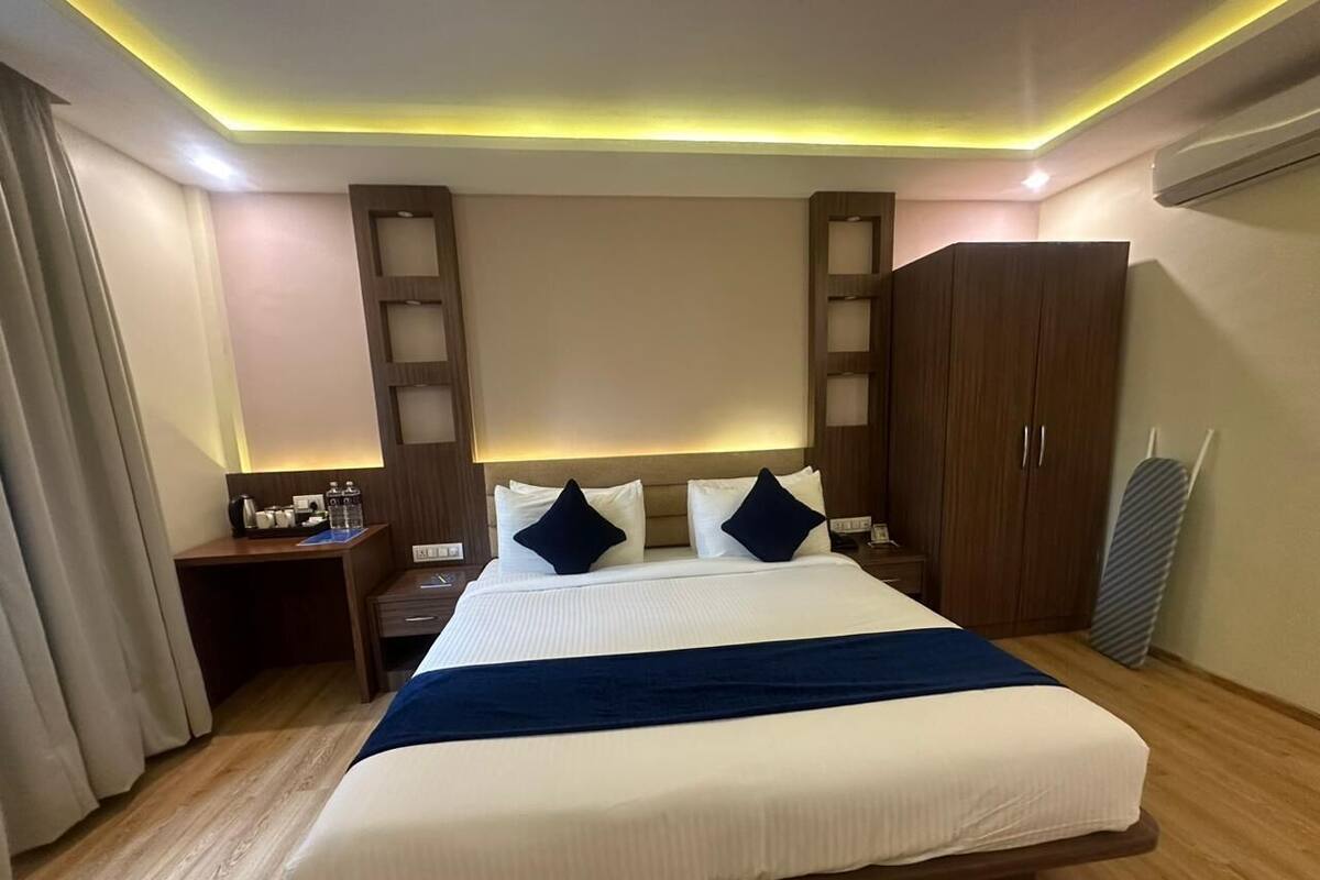 Una habitación de hotel con una cama grande, cabecero de madera, mesitas de noche, un escritorio y un armario.