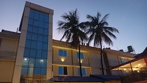 A modern building with a glass facade, palm trees, and a balcony with outdoor seating.