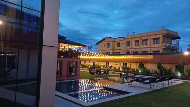 A modern hotel with a swimming pool, outdoor seating, and a well-lit balcony area.