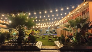 An outdoor seating area with string lights, palm trees, and a water feature.