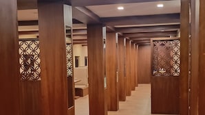 A corridor with wooden pillars and patterned metal screens, leading to a series of rooms.
