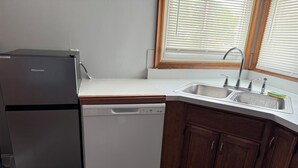 Una cocina compacta con lavavajillas, pileta integrada, muebles de madera y una ventana con persianas.