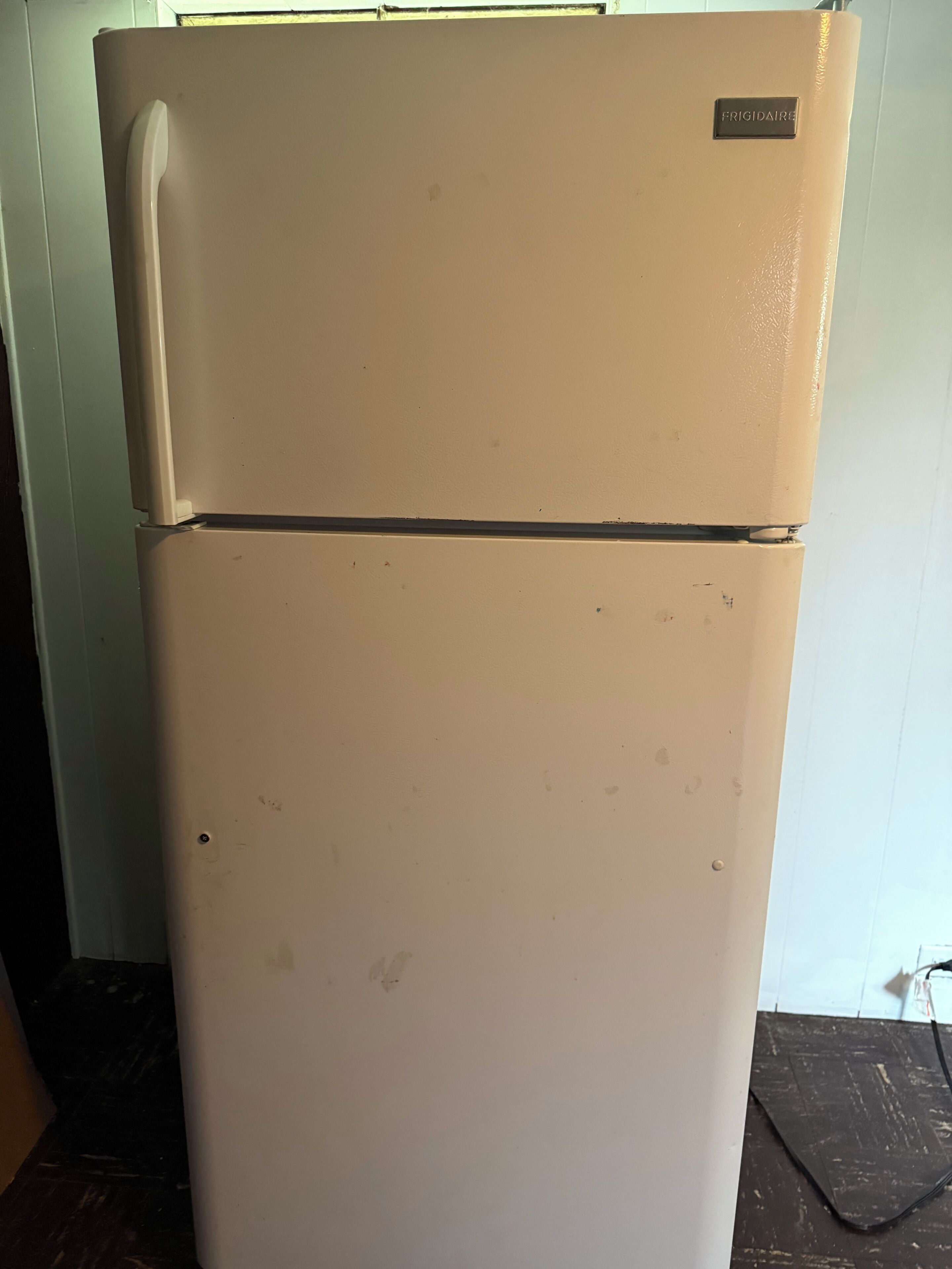 A beige refrigerator with visible wear and a label reading "FRIGIDAIRE".