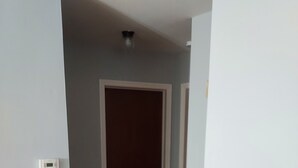 Un pasillo con suelo de madera, una puerta blanca y un interruptor de luz en la pared.