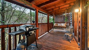Une terrasse en bois avec un barbecue et une bouteille de propane, un banc et une vue sur les arbres.