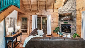 Un intérieur de chalet chaleureux avec une cheminée en pierre, des poutres en bois, un canapé en cuir et un coin repas.