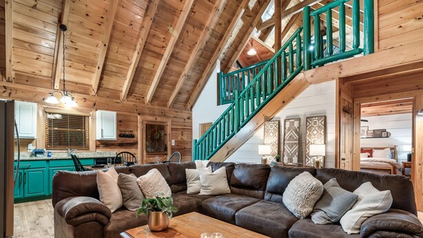 Un salon spacieux avec un grand canapé d’angle en cuir marron, une table basse en bois et un escalier doté de rampes vertes.