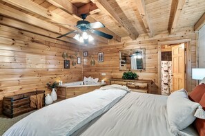 A wooden cabin bedroom with a bed, a vanity with a mirror, a ceiling fan, and a small window. - Smoky Mtn Fall Foliage Cabin – Hot Tub, Indoor Pool, Near Dollywood, Sleeps 6 (Sevierville)