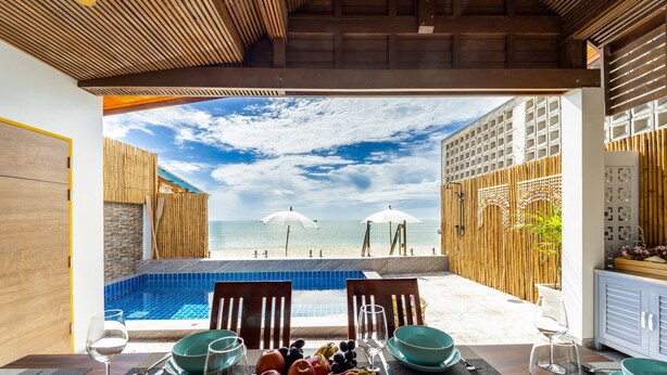 A dining table with a view of the beach and pool, wooden furniture, and a fruit bowl. - Beach Front Villa with 3 Bedrooms - CA3 (Cha-am)