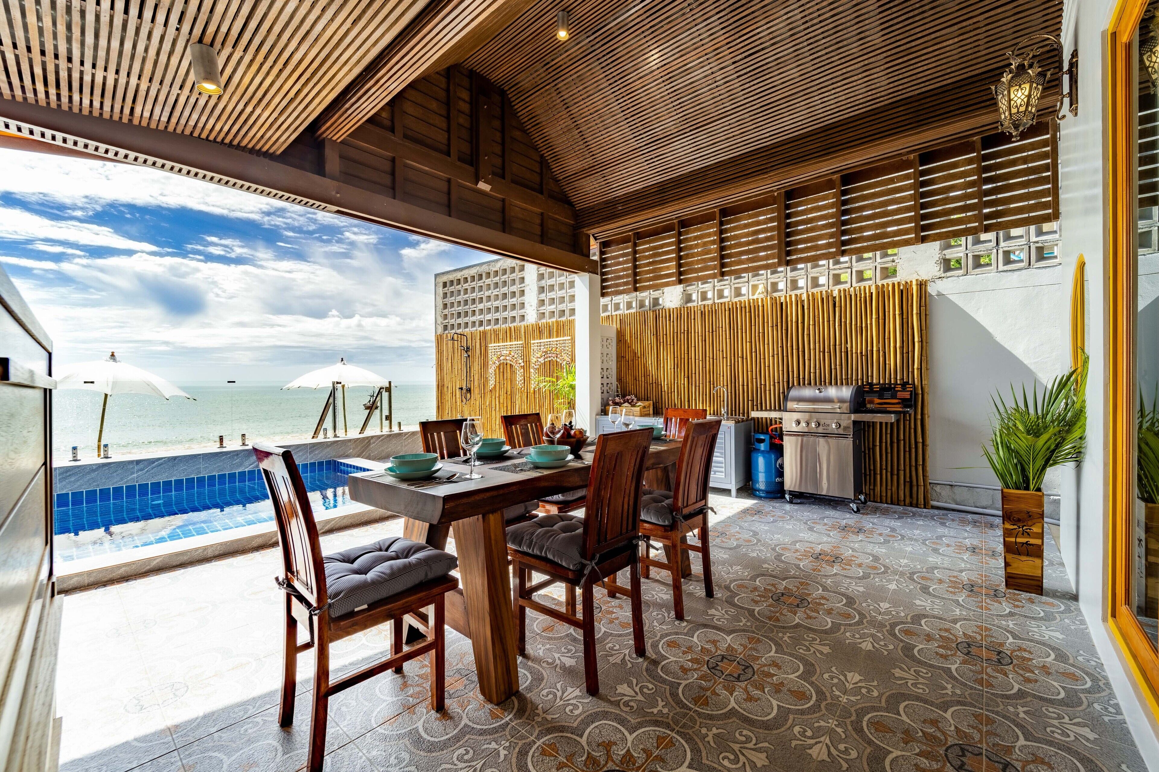 A dining area with a view of the ocean, a pool, and a grill.