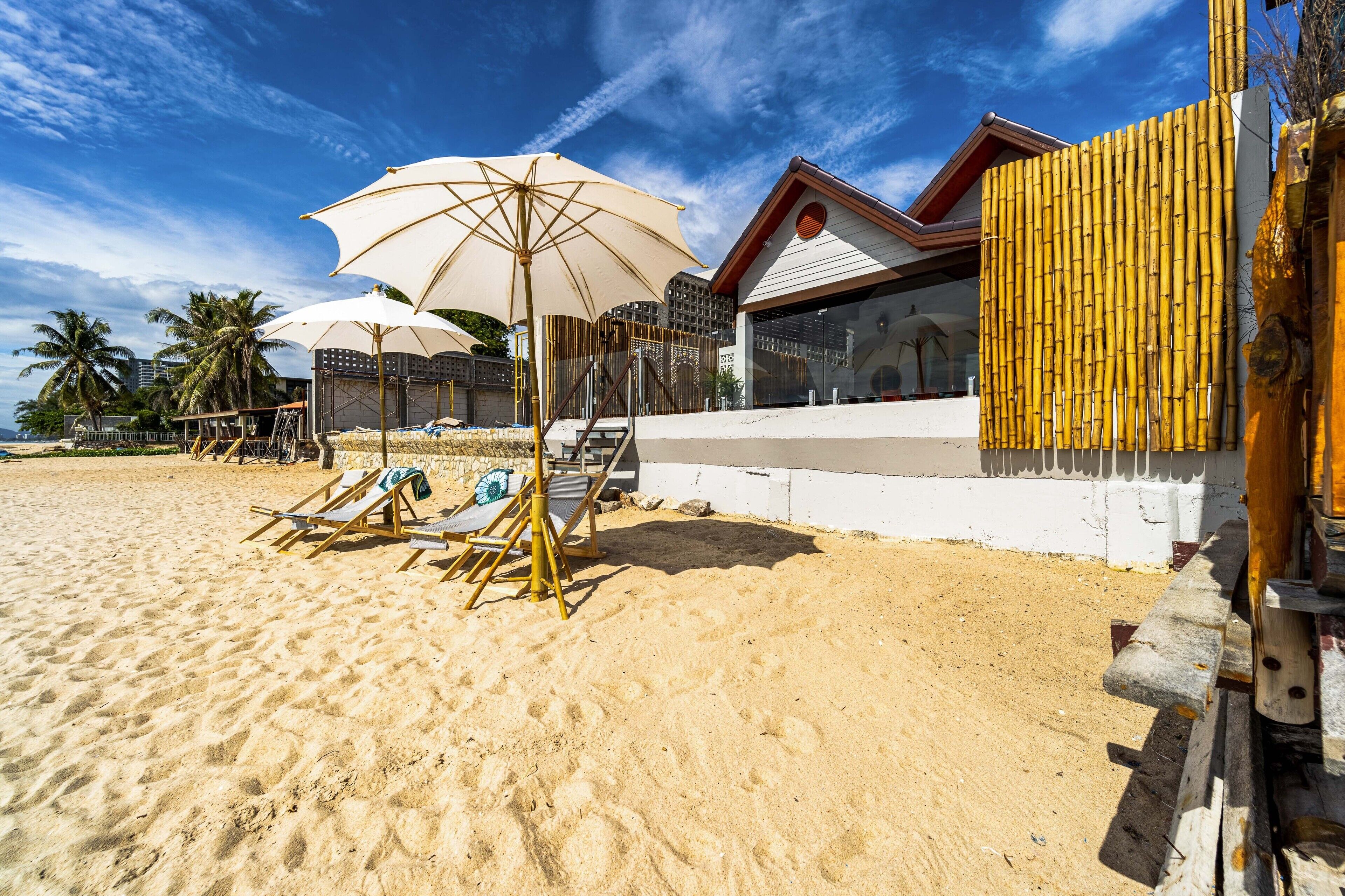 A beachside hotel with sun loungers and umbrellas, a bamboo fence, and a pool area.