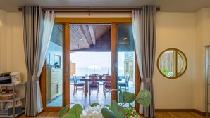 A room with a wooden floor, a dining area with a table and chairs, and a view of the sea through a glass door. - Beach Front Villa with 3 Bedrooms - CA3 (Cha-am)