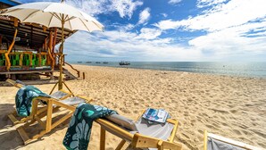 A beach with wooden lounge chairs and a large umbrella, a wooden structure with a sign, and a view of the sea with boats. - Beach Front Villa with 3 Bedrooms - CA3 (Cha-am)