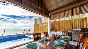 A dining area with a view of the beach and ocean, a pool, and a kitchen area with a grill. - Beach Front Villa with 3 Bedrooms - CA3 (Cha-am)