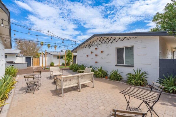 A courtyard with outdoor seating, a white building with decorative elements, and a clear sky.