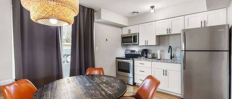A modern kitchen with white cabinets, stainless steel appliances, and a dining area with a round table and two chairs.