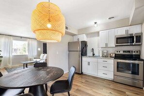 A modern kitchen with stainless steel appliances, a dining area with a round table and chairs, and a large window providing natural light.