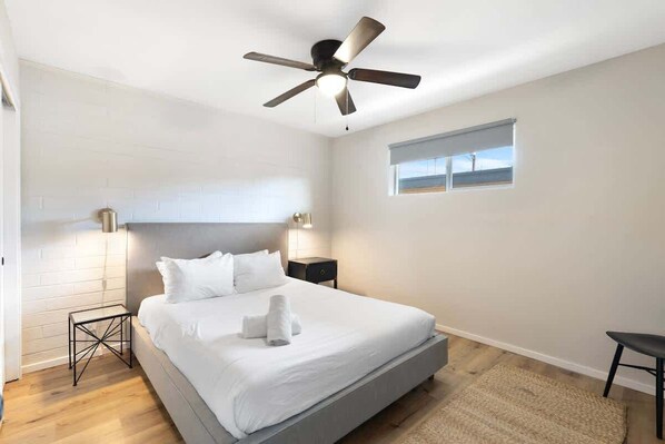 A bedroom with a bed, a ceiling fan, a nightstand, a window, and a small table.