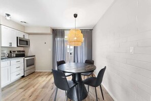 A compact kitchen with white cabinets, a microwave, an oven, and a dining table with four chairs.
